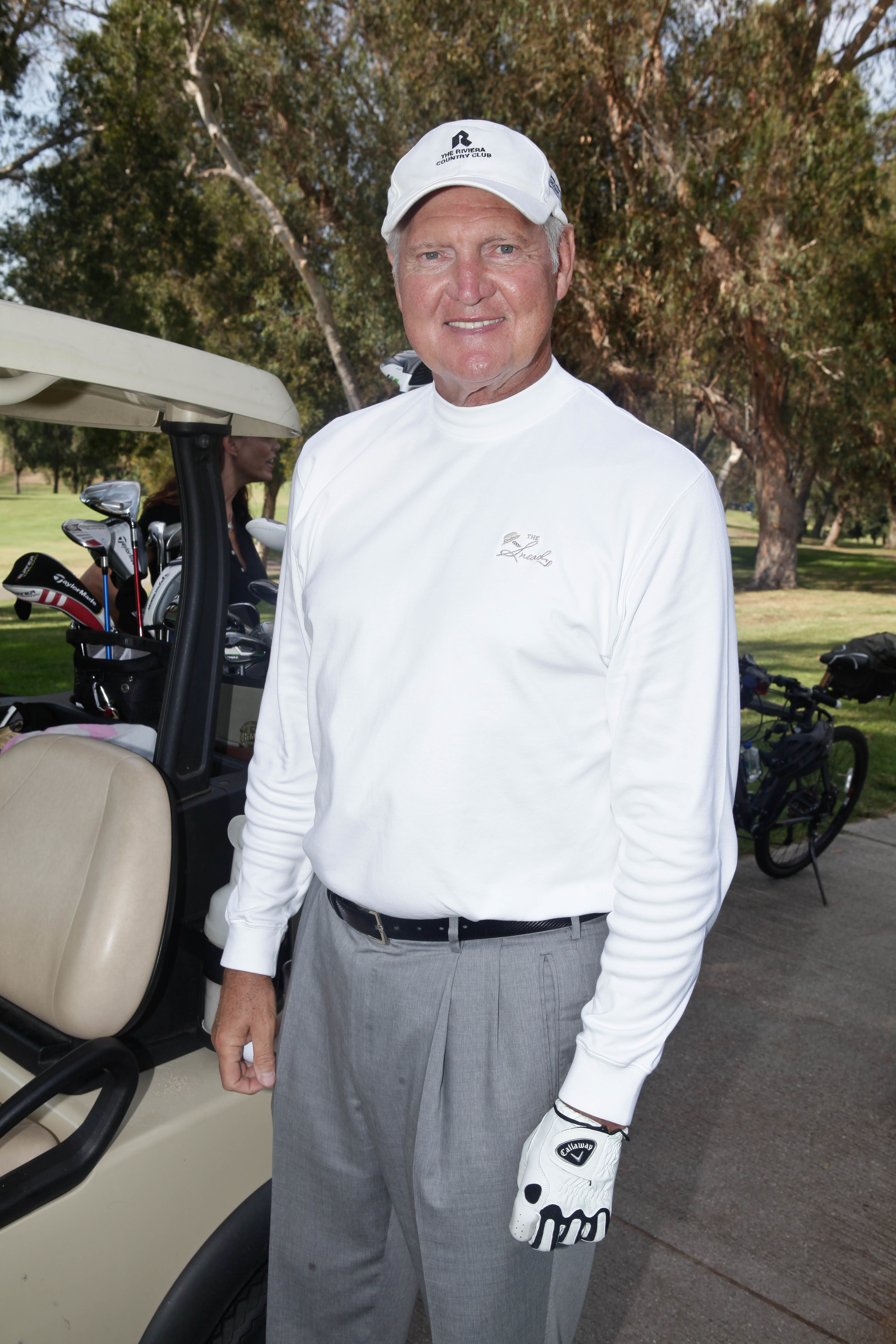 Golfer standing with golf cart, wearing a white long-sleeve shirt, gray pants, and glove, ready to play