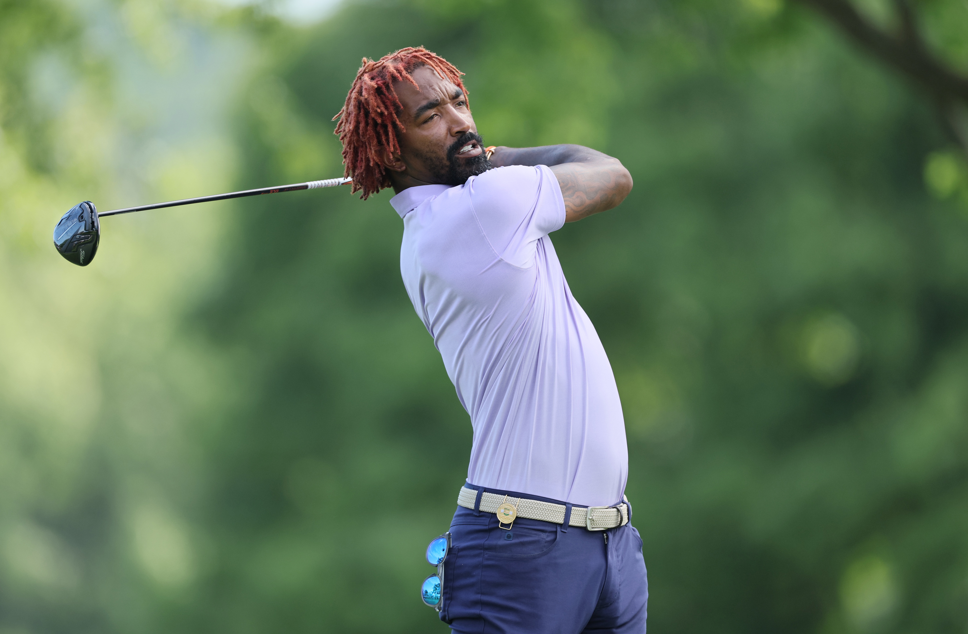 Golfer mid-swing on a course, dressed in a polo shirt and trousers, focused on the ball