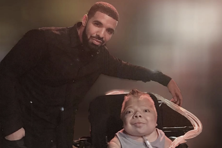 Drake stands next to a young fan in a wheelchair, both smiling at the camera