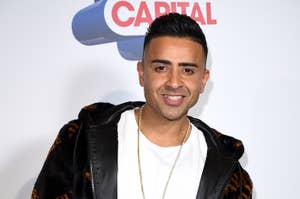 Jay Sean posing with a peace sign, wearing a bomber jacket with fur-like detailing and a chain necklace
