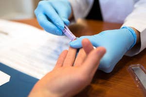 医療従事者が手袋をはめ患者の指から血液サンプルを採取している様子。