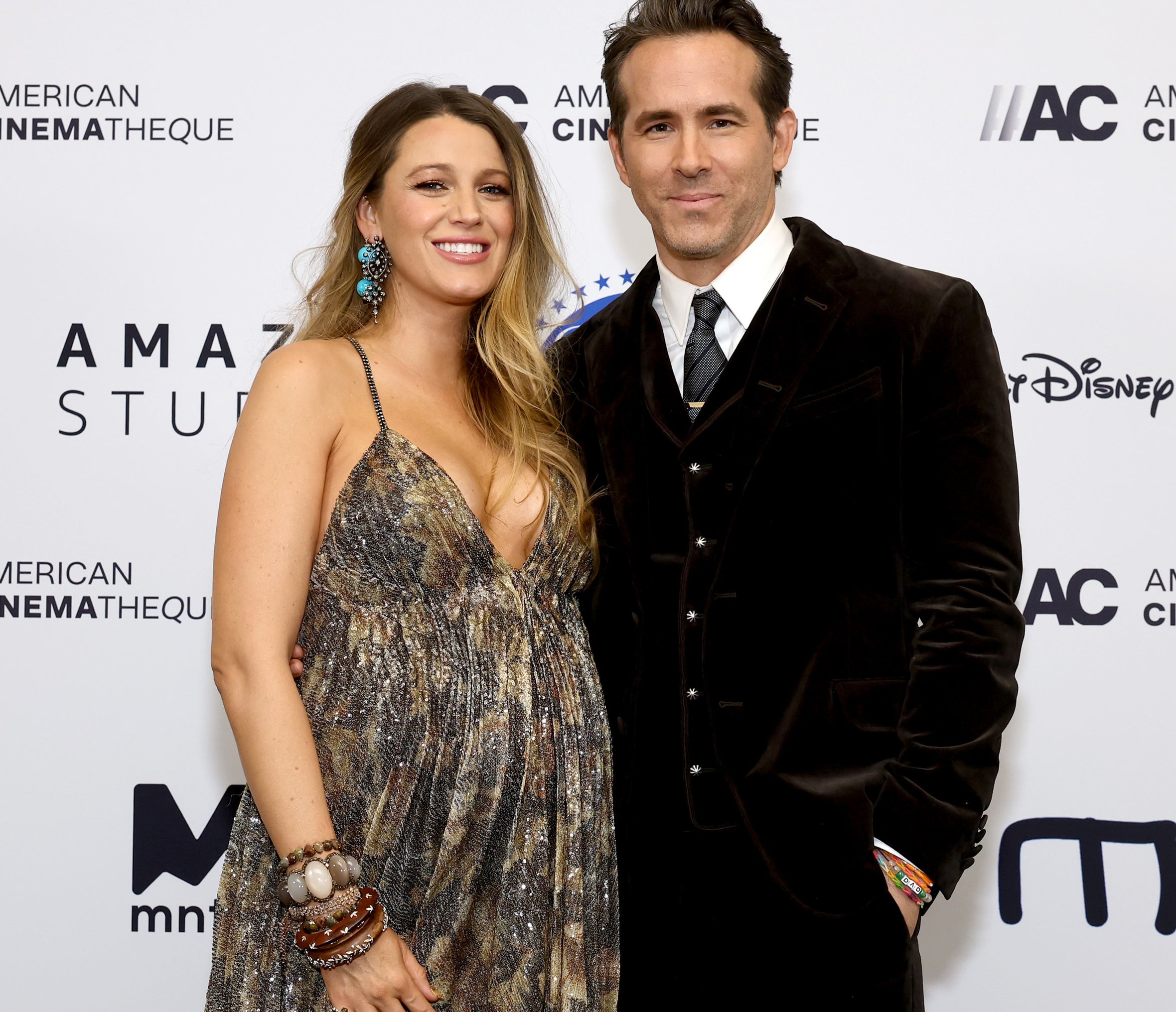 Blake Lively in a patterned dress with Ryan Reynolds in a suit, both smiling on the red carpet