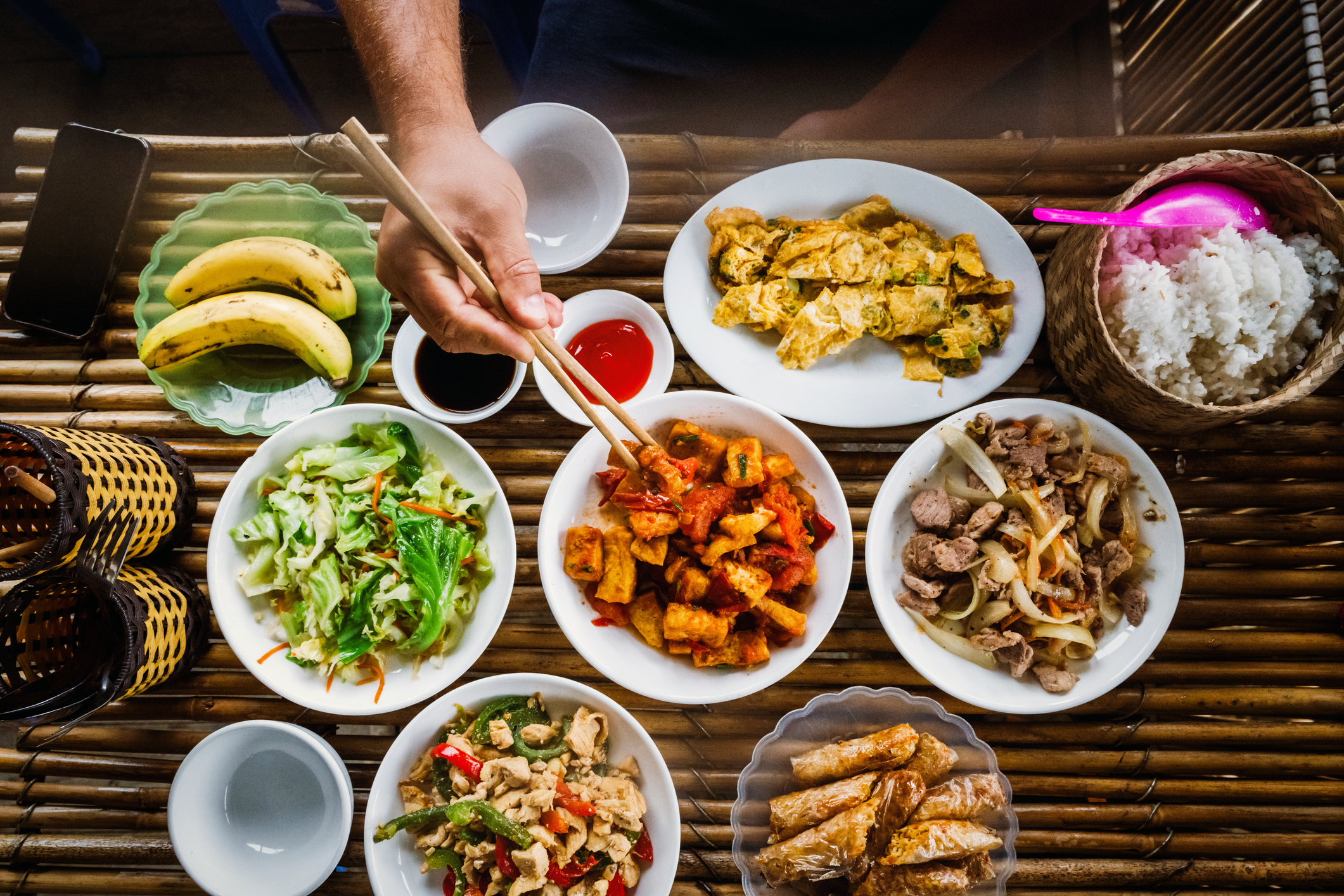 Person eating a traditional Asian meal with various dishes, including rice, vegetables, and meat
