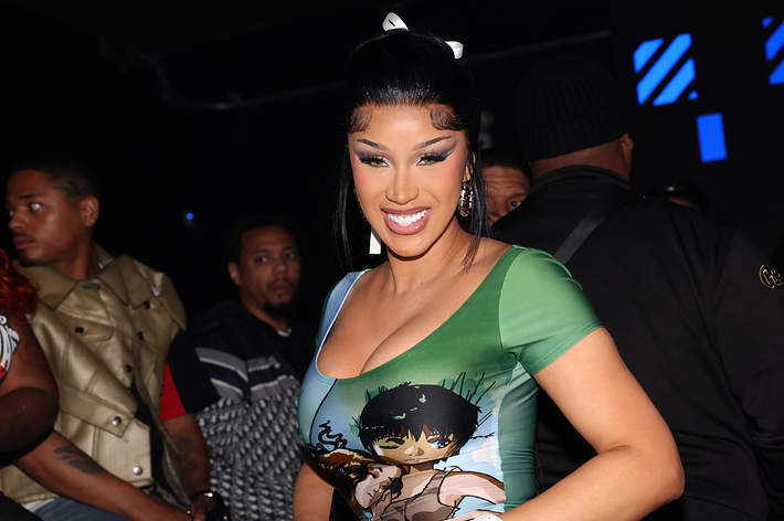 Cardi B at event wearing a graphic tee with an anime character, accessorized with a bow in their hair