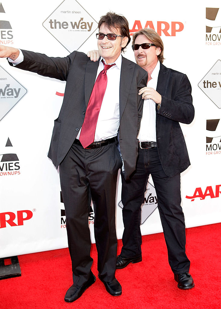 Two men in suits posing playfully, one pointing and smiling, the other peeking from behind