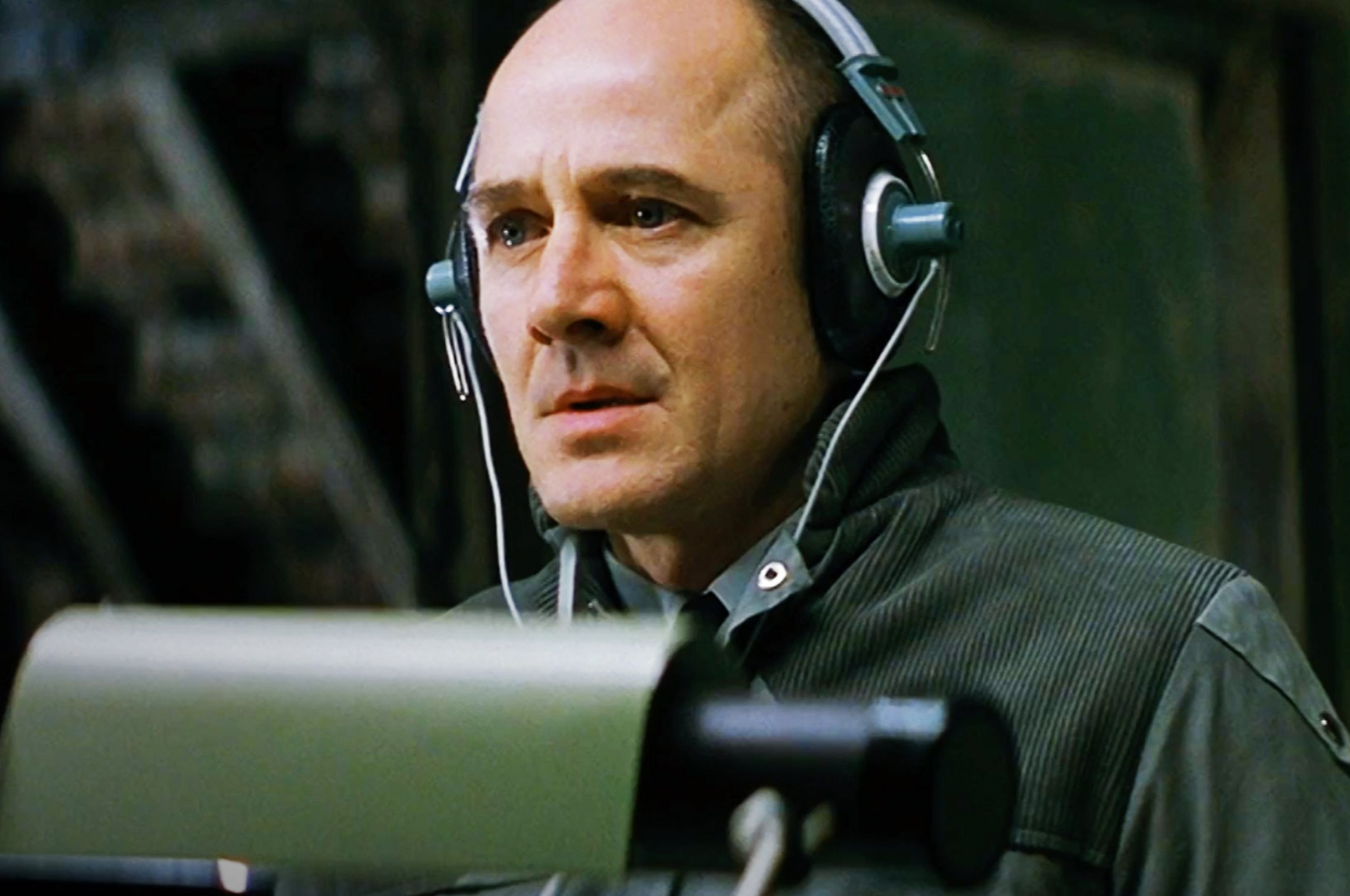 Kevin Spacey in character wearing headphones, in front of a microphone, looking focused