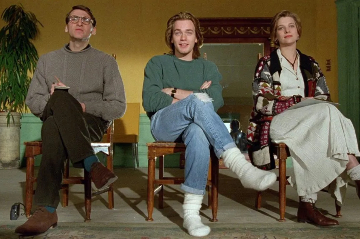 Three actors sit side by side in director&#x27;s chairs, likely a behind-the-scenes shot from a film set
