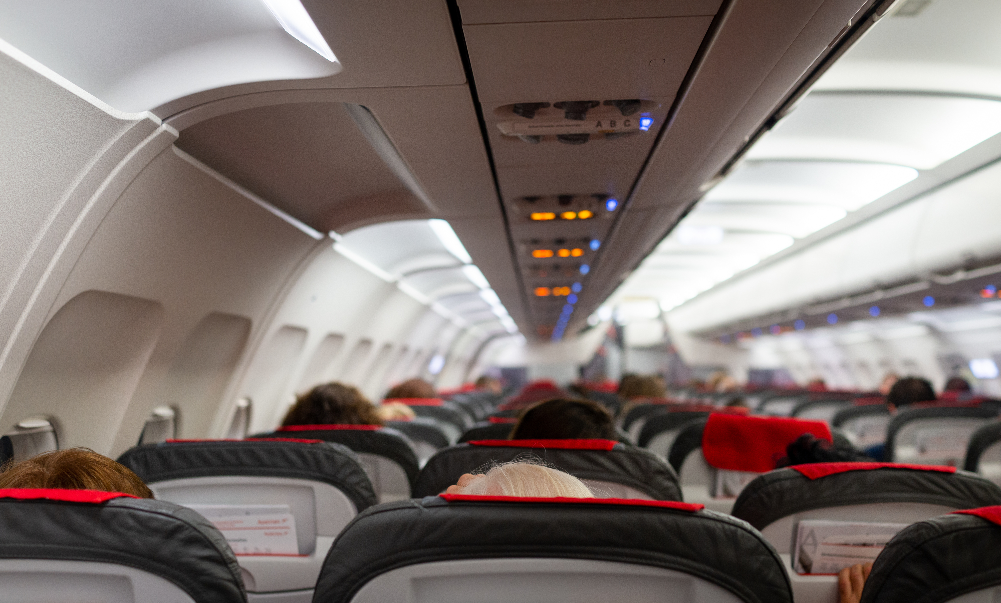 Interior of an airplane with passengers seated, looking towards the front of the cabin