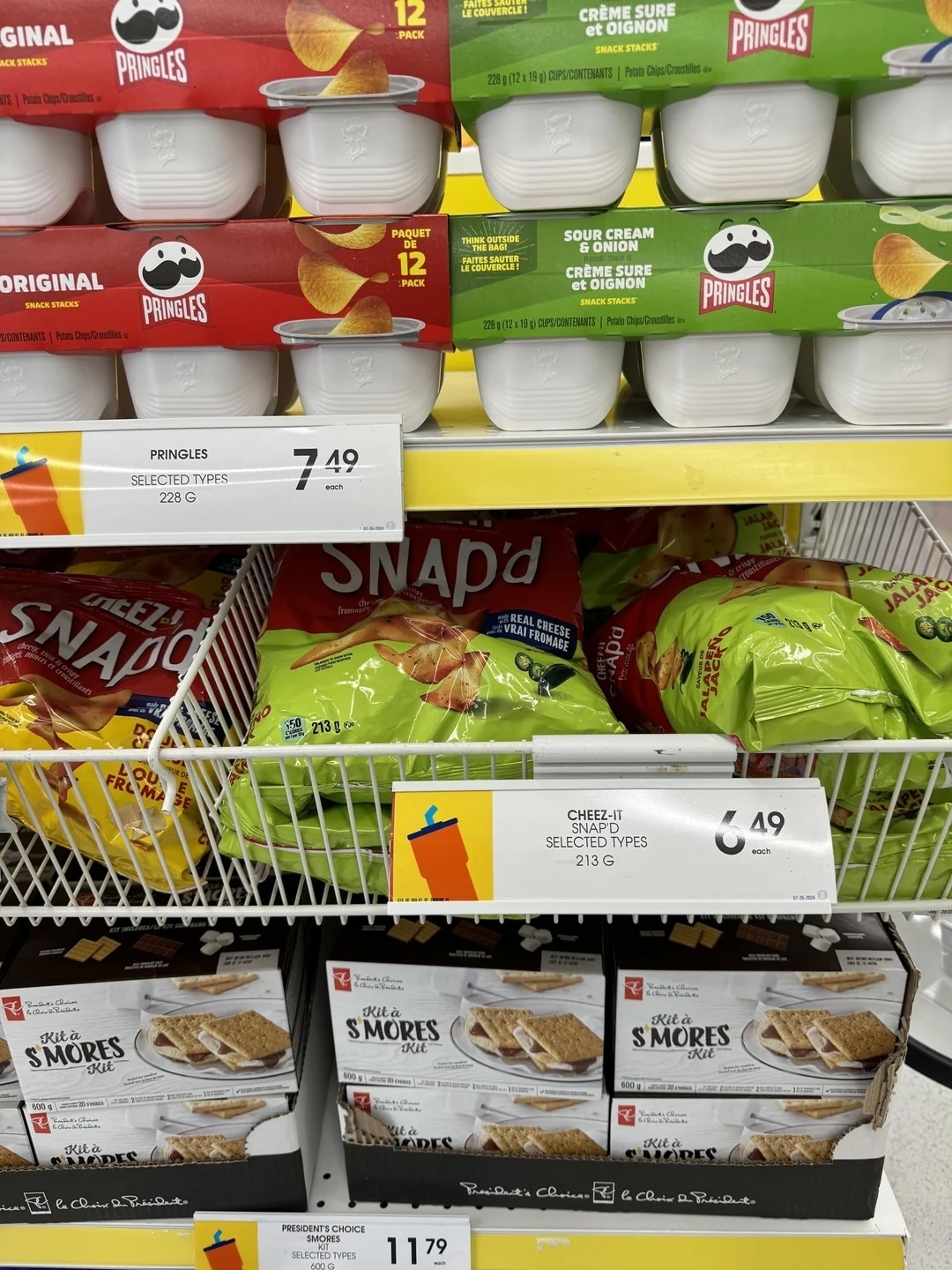 Shelves stocked with assorted snack items including Pringles, Cheez-It Snap'd, and S'mores kit. Prices are displayed