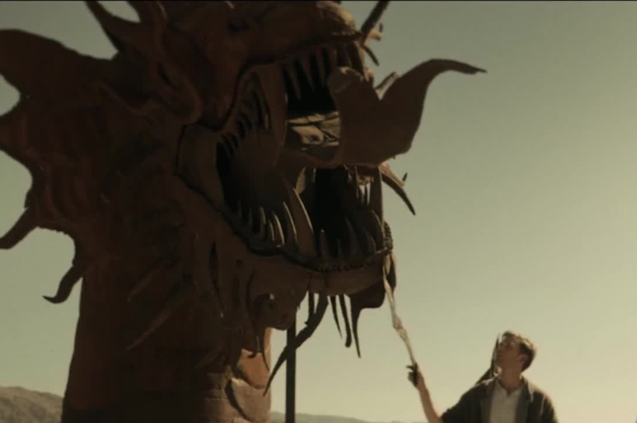 Person in desert landscape holding a staff faces a large dragon-like creature