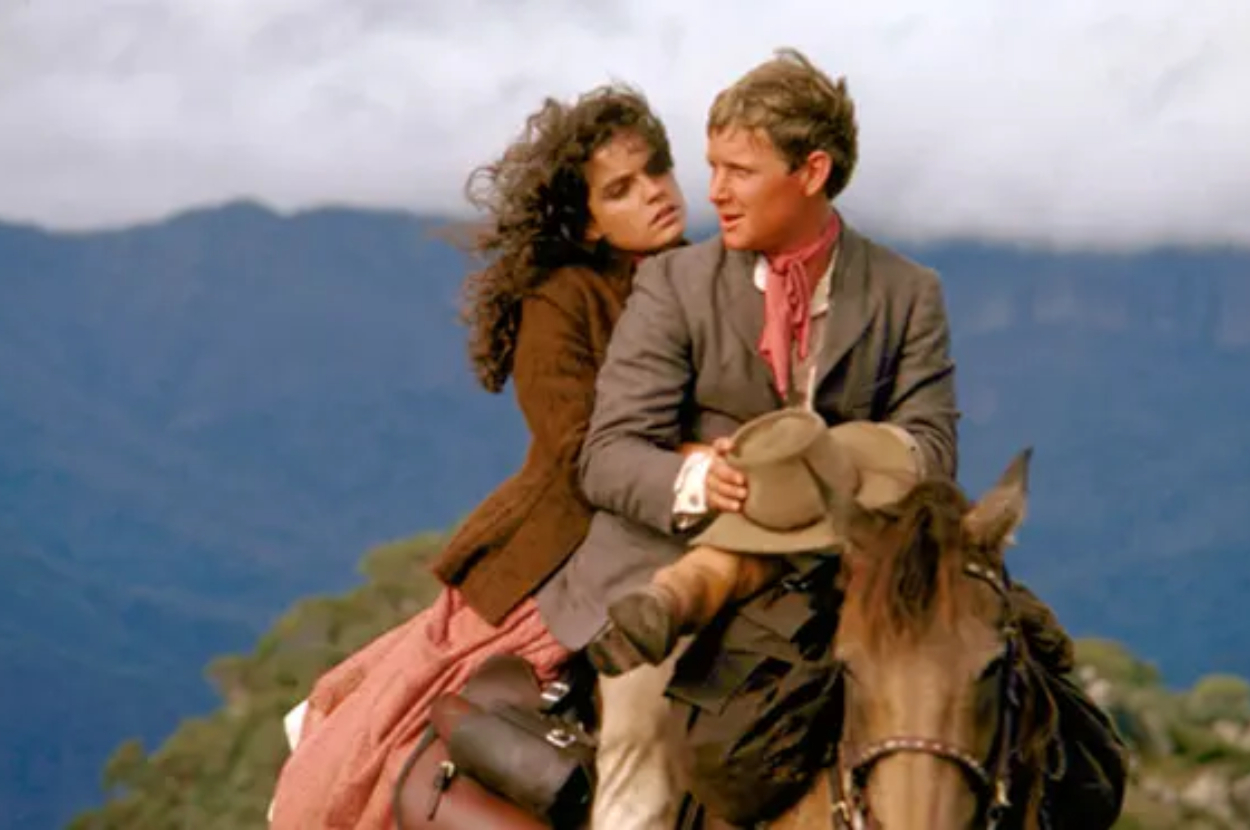 Two characters in historical attire on a horse, man in a jacket and woman in a dress