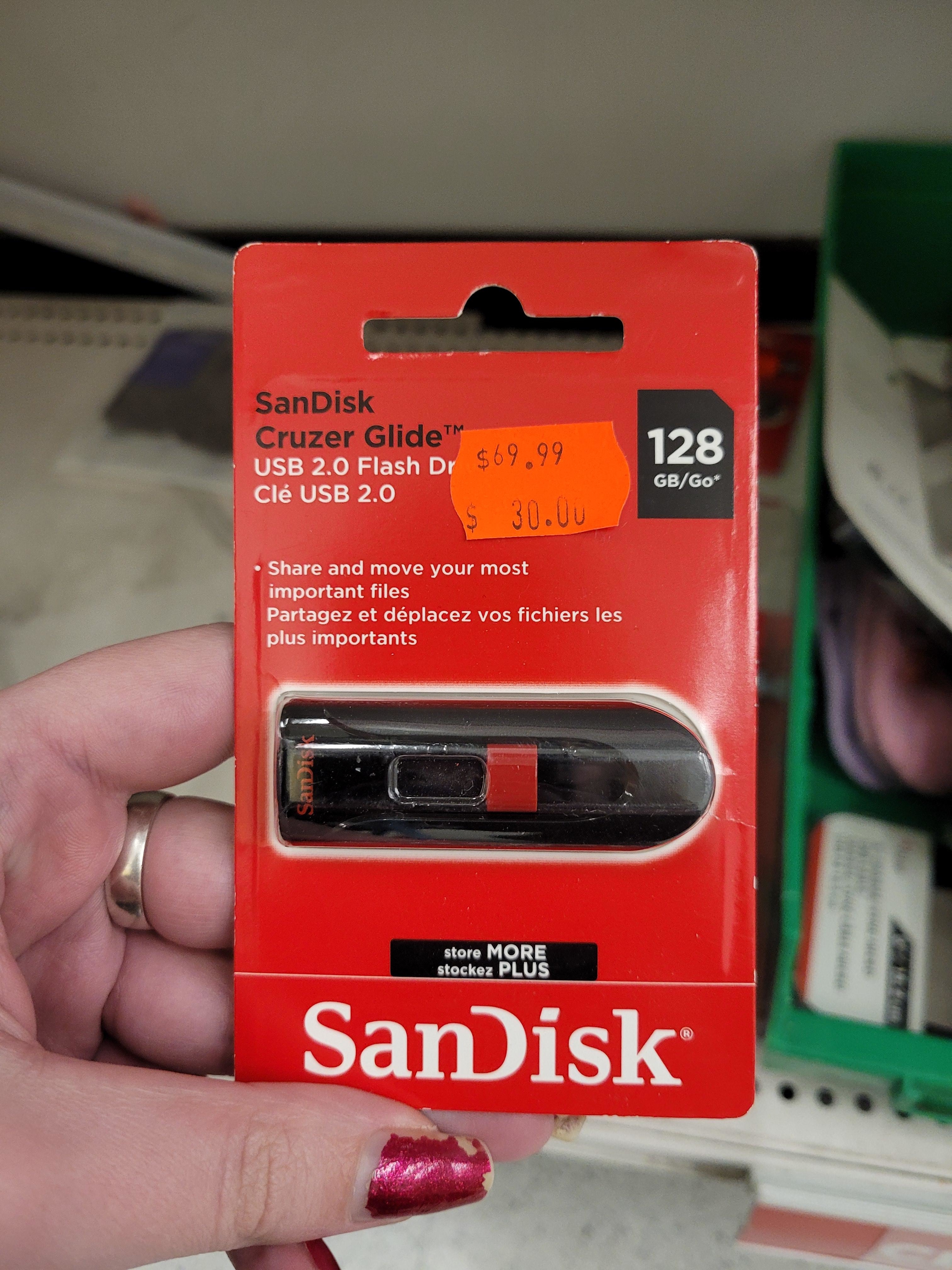 A hand holding a SanDisk Cruzer Glide USB flash drive packaging with a price tag of $69.99, on sale for $30.00