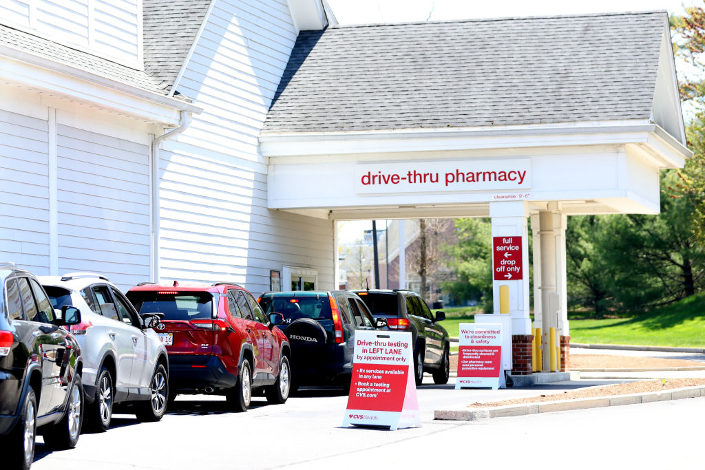 Vehicles lined up at a drive-thru pharmacy with informational signs visible