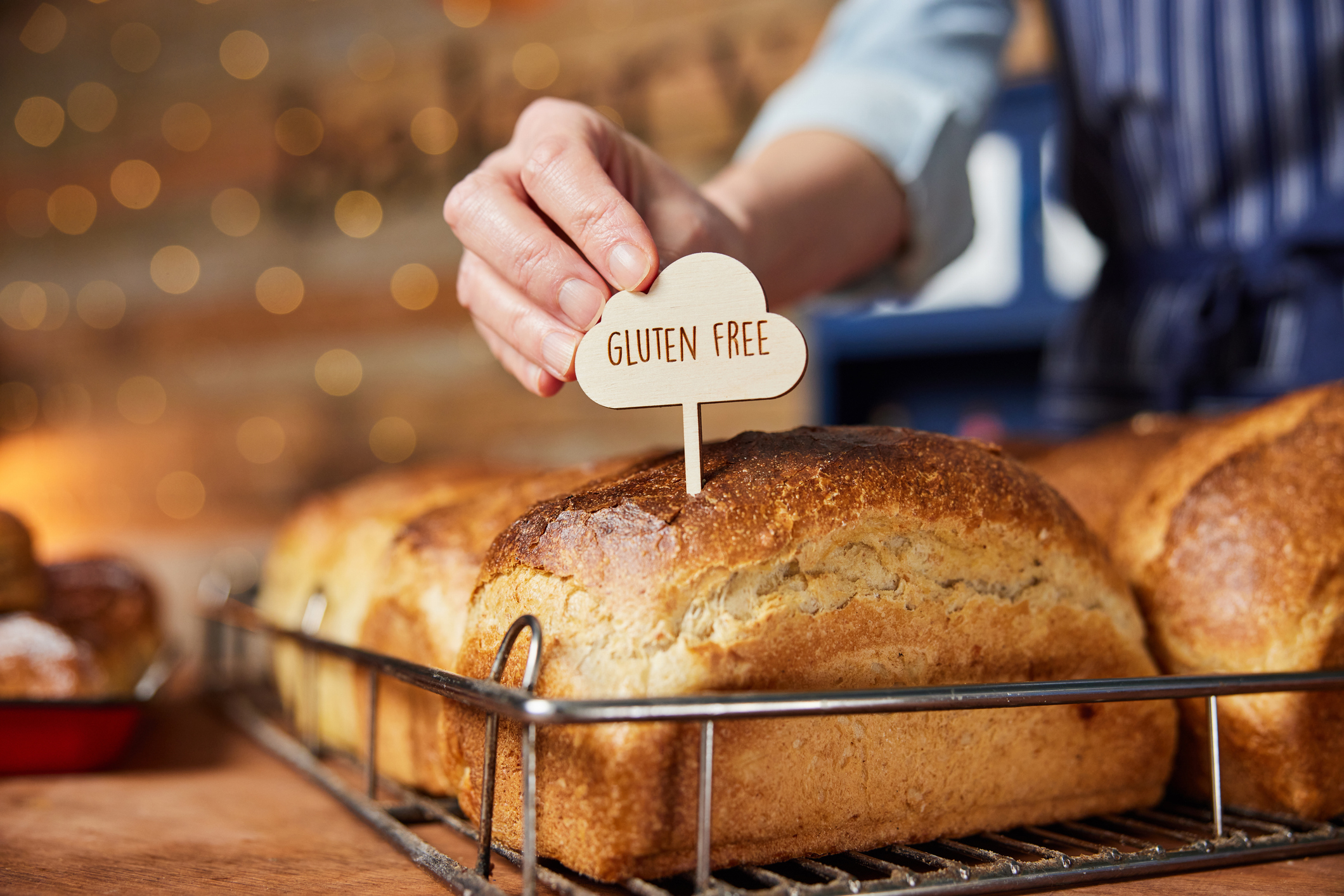 Hand placing a &quot;gluten-free&quot; sign on freshly baked loaves of bread in a bakery display