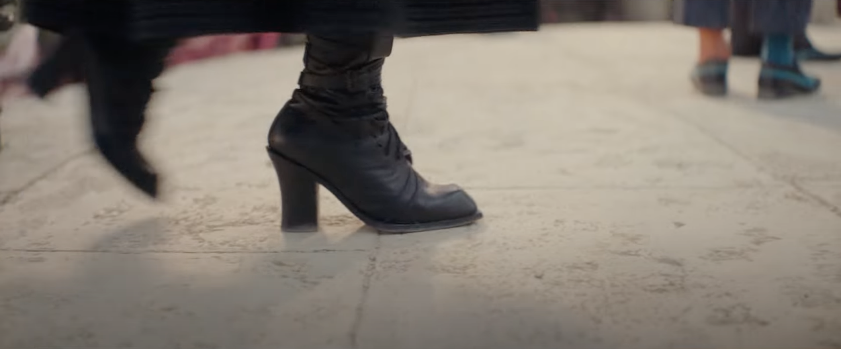 Person in heeled boots walking, partial view of others' lower bodies in background