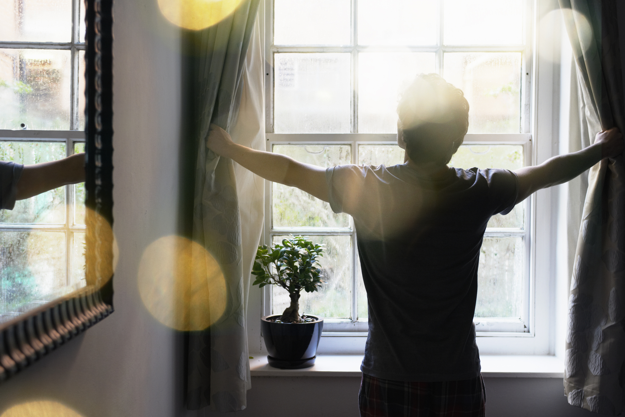 Person opening curtains to look out window, backlit with a warm glow, suggesting a new beginning or fresh start