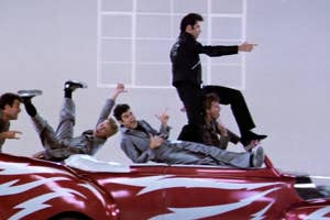 Animated character Danny Zuko and the T-Birds sing atop a red convertible in Grease