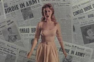 Woman in a vintage dress standing in front of a backdrop with multiple newspaper headlines