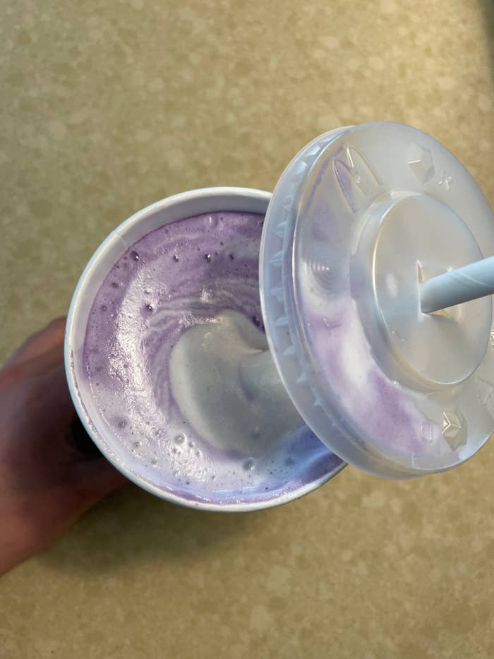 Hand holding a cup with a straw, filled with a purple blended beverage