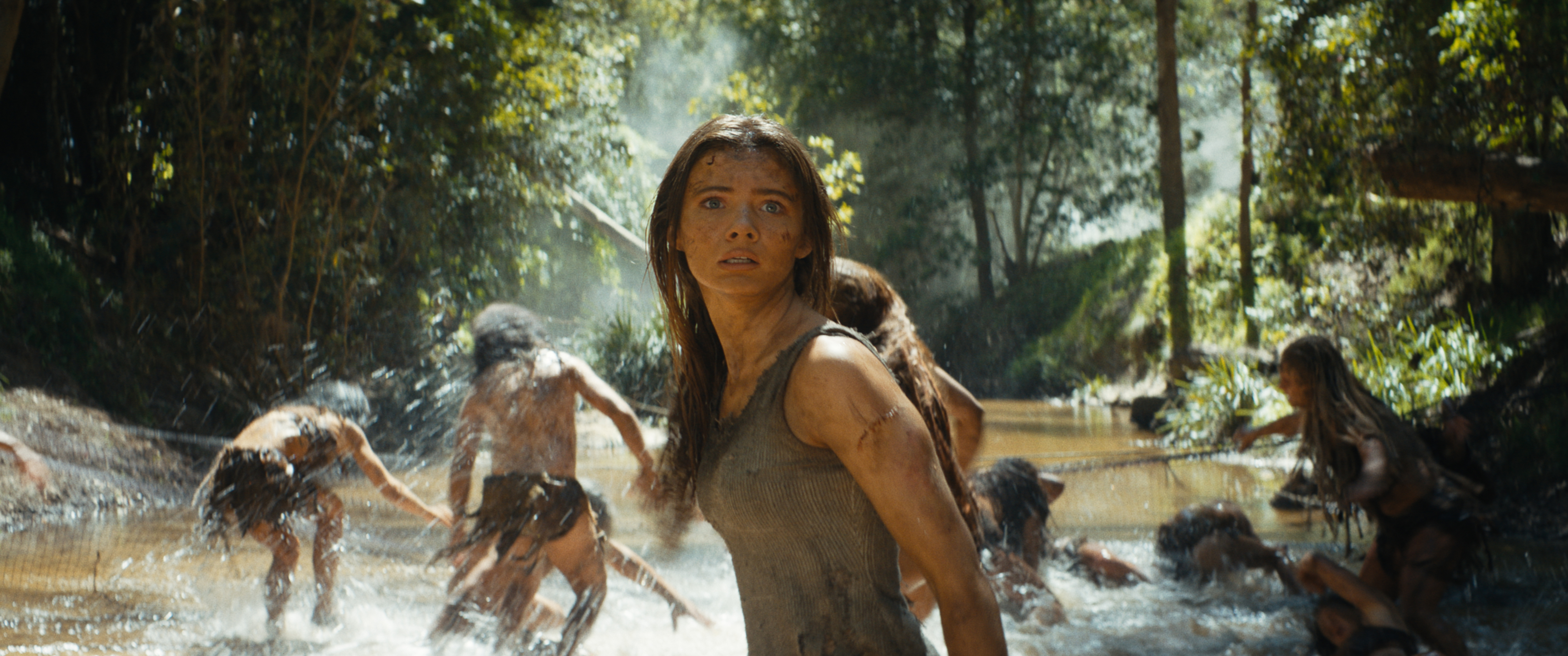 Woman in prehistoric attire looks alarmed with others in background. Scene from a film