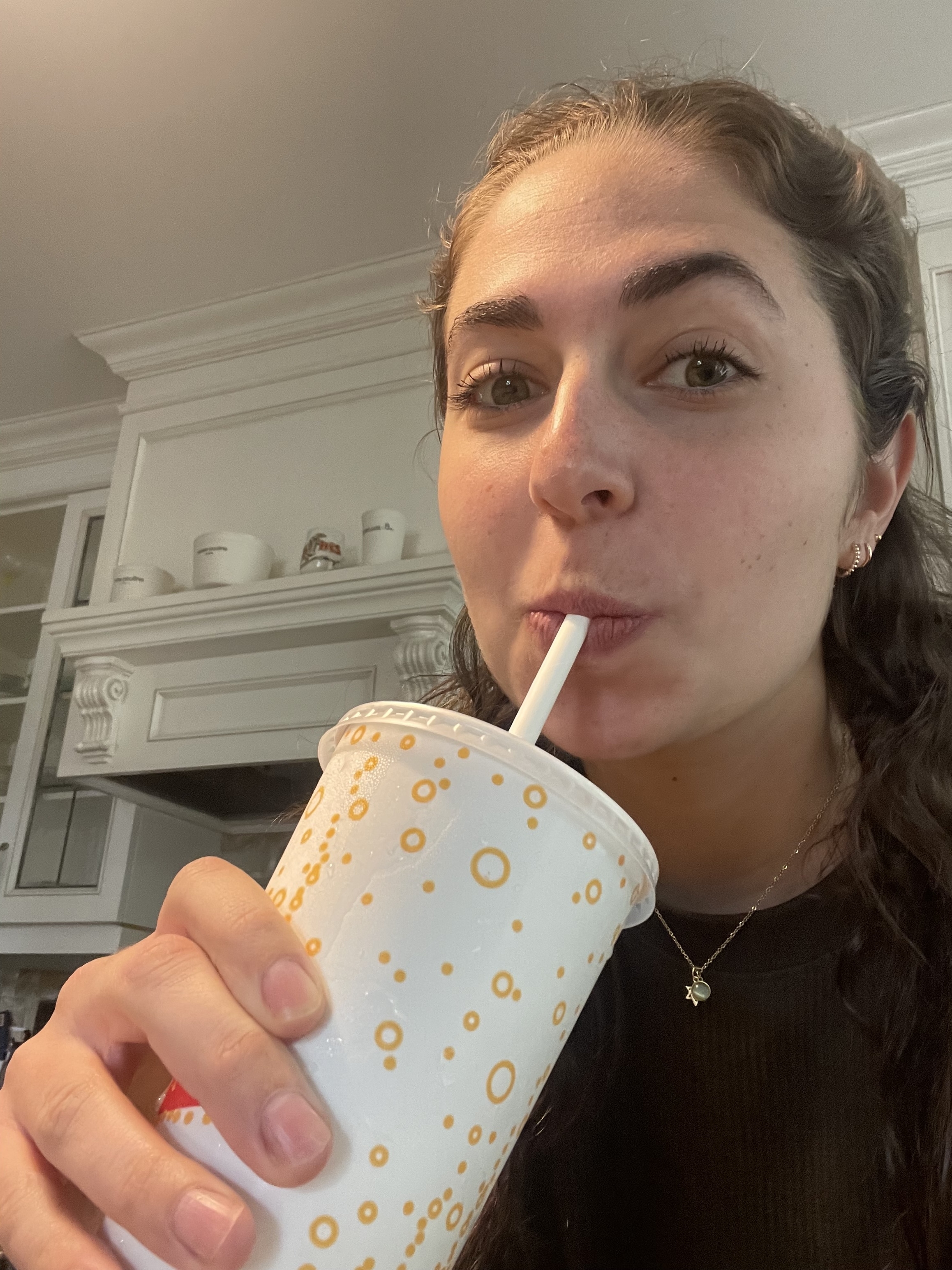Woman sipping from a straw in a patterned cup, casual attire, in a kitchen setting