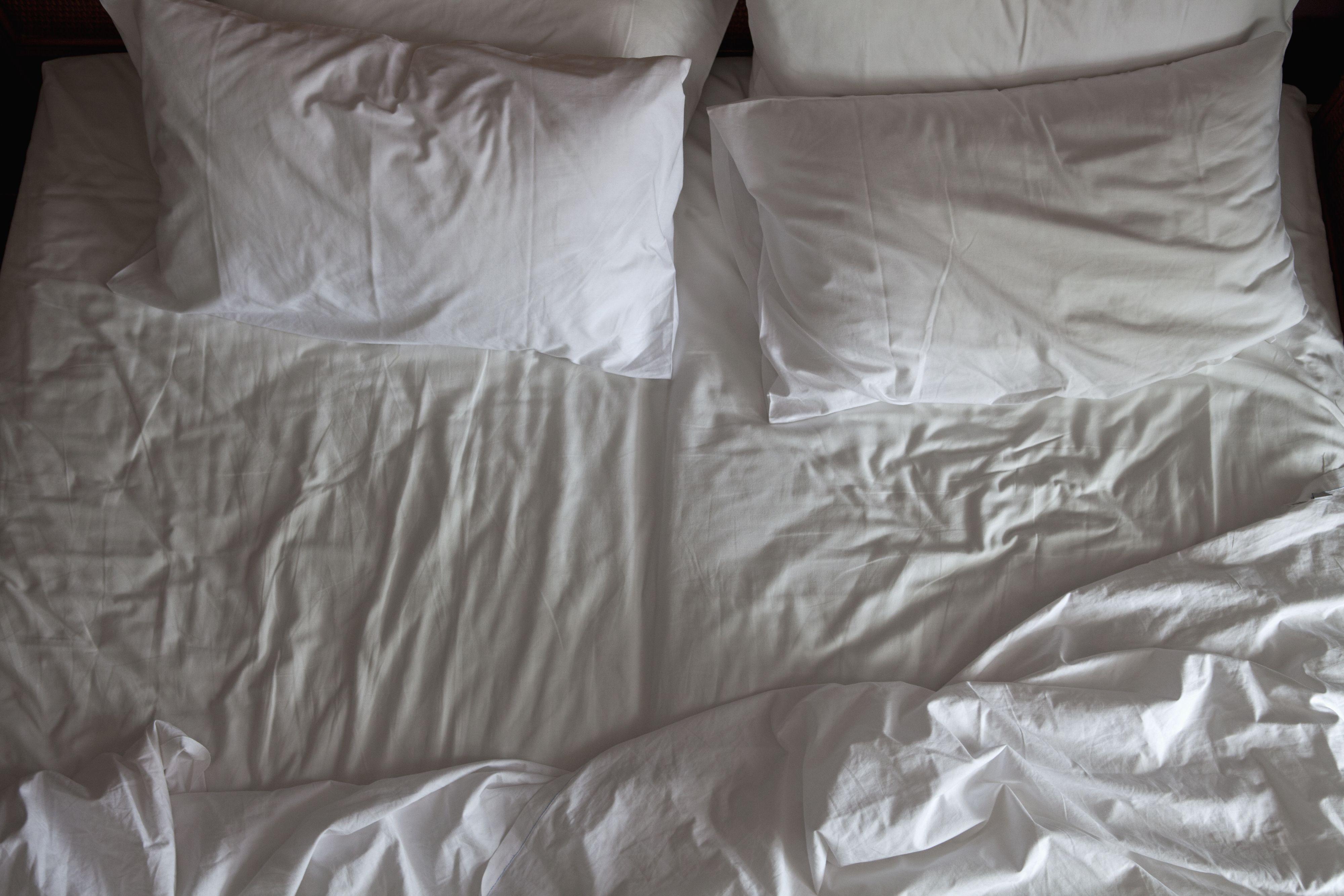 Unmade bed with disheveled white sheets and four pillows
