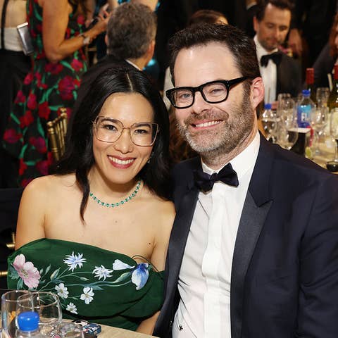 Couple smiling at a table during an event, man in a bow tie and woman in a green dress with floral pattern