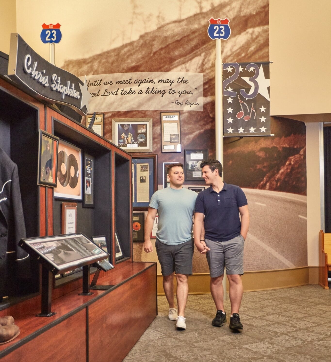 Two men walking past a Chris Stapleton exhibit, engaged in conversation