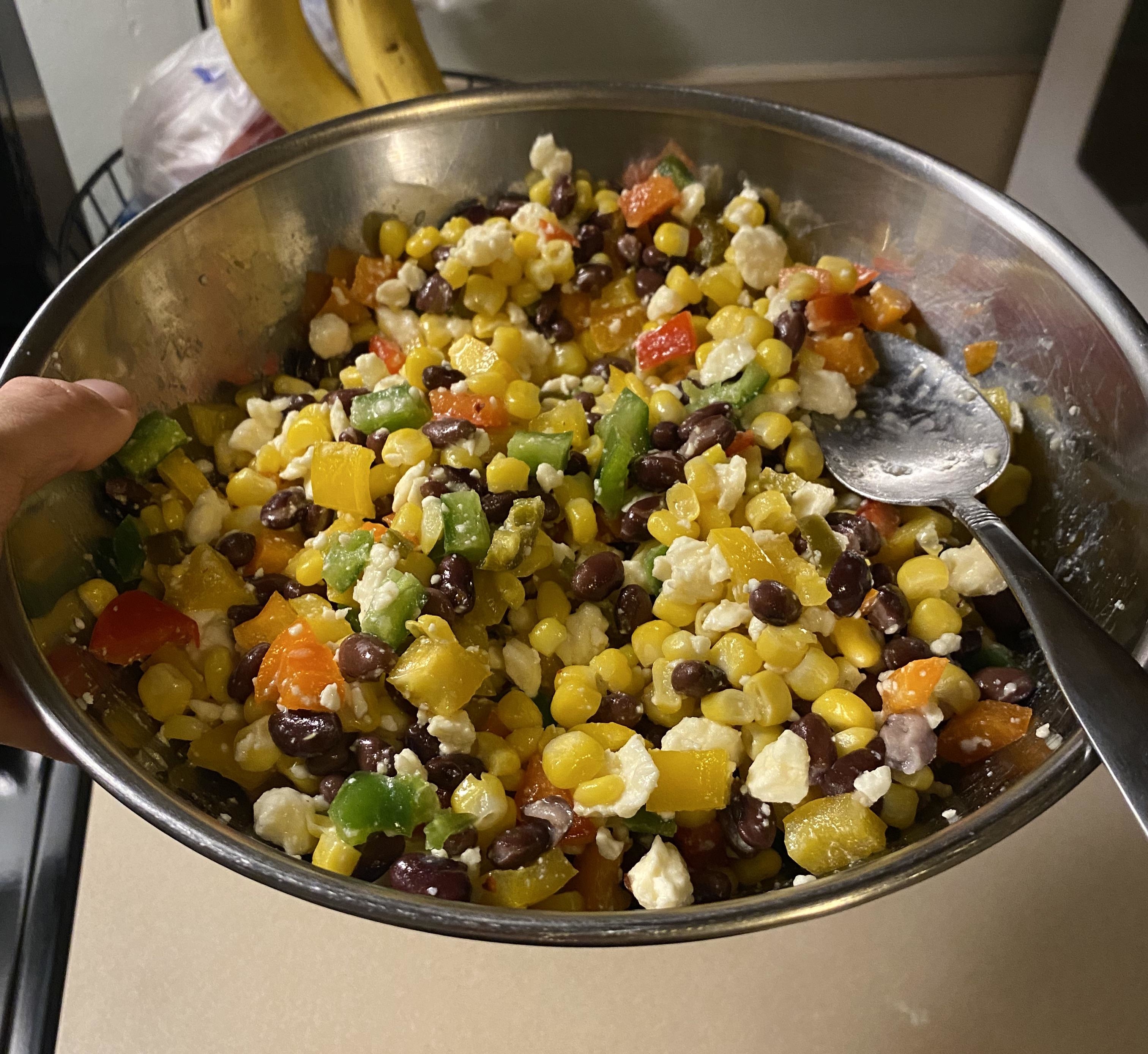 A bowl of mixed salad with various vegetables and beans, being stirred with a spoon