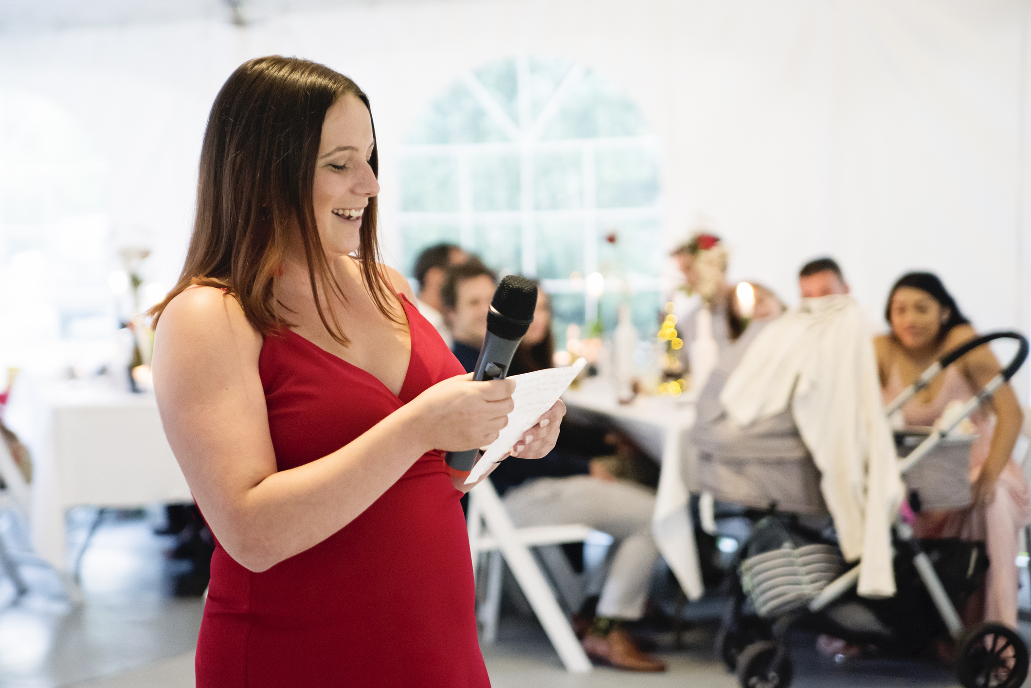 Woman reading a card at an event, guests in the background, expressing joy and surprise