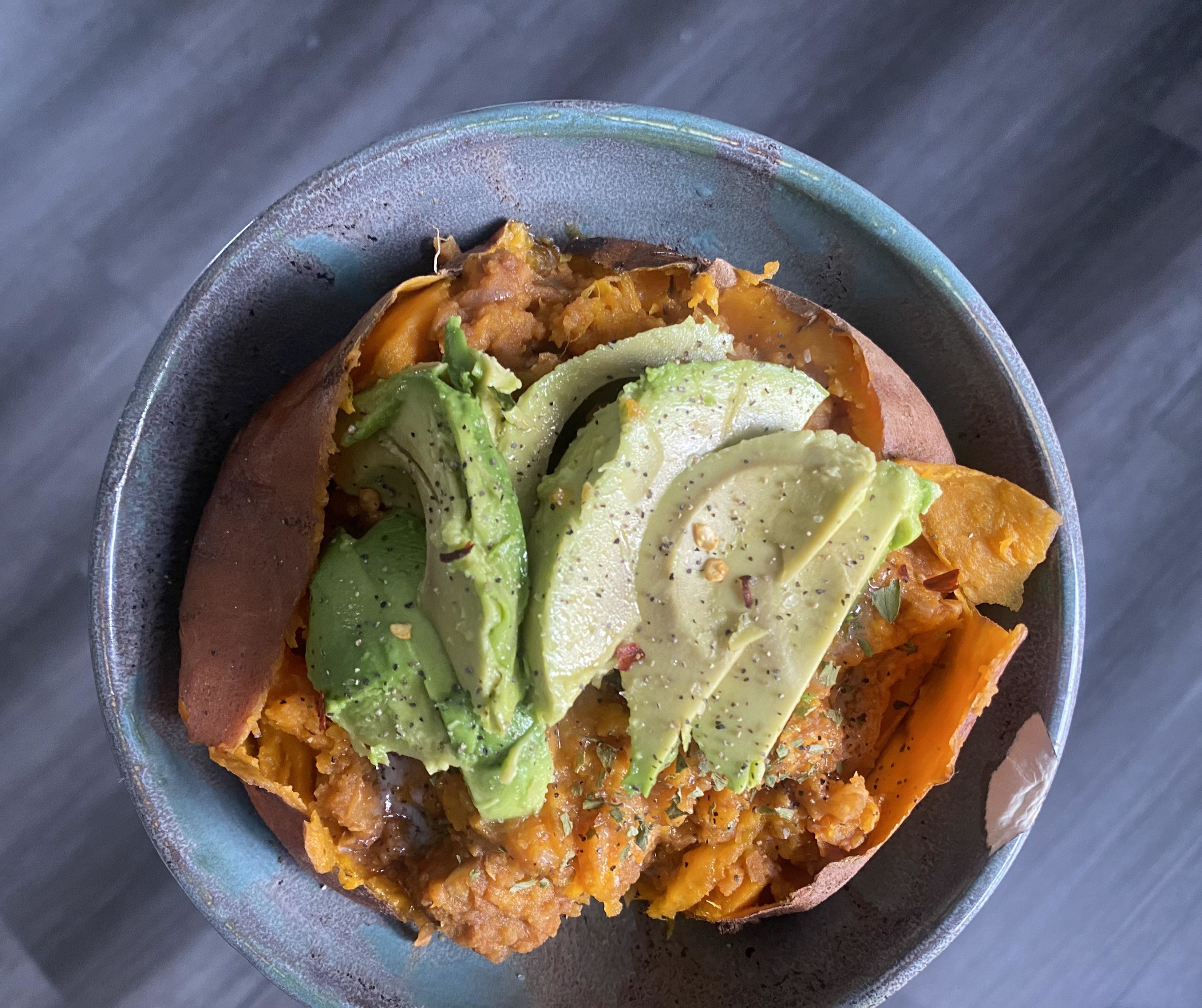 A bowl of sweet potato nachos topped with avocado slices and a sprinkle of herbs