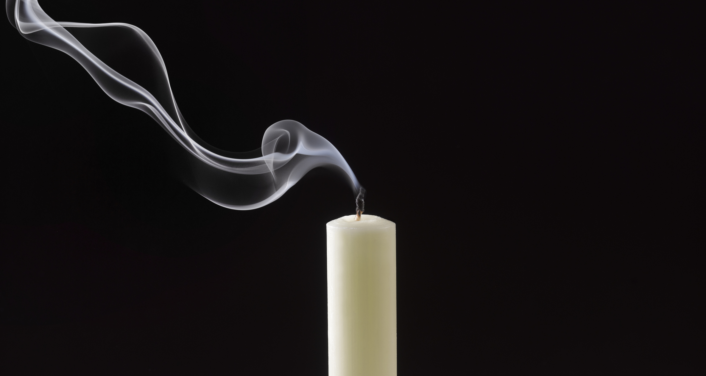A single candle with a wisp of smoke rising from its extinguished wick against a dark background