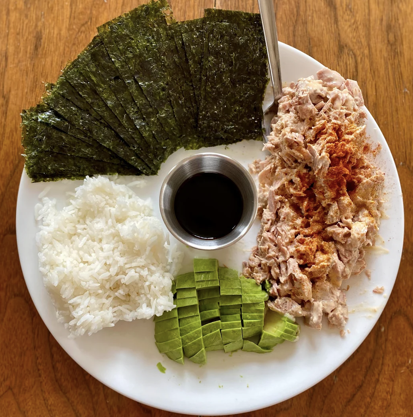 Plate with rice, tuna, avocado, seaweed, and soy sauce, arranged for DIY sushi