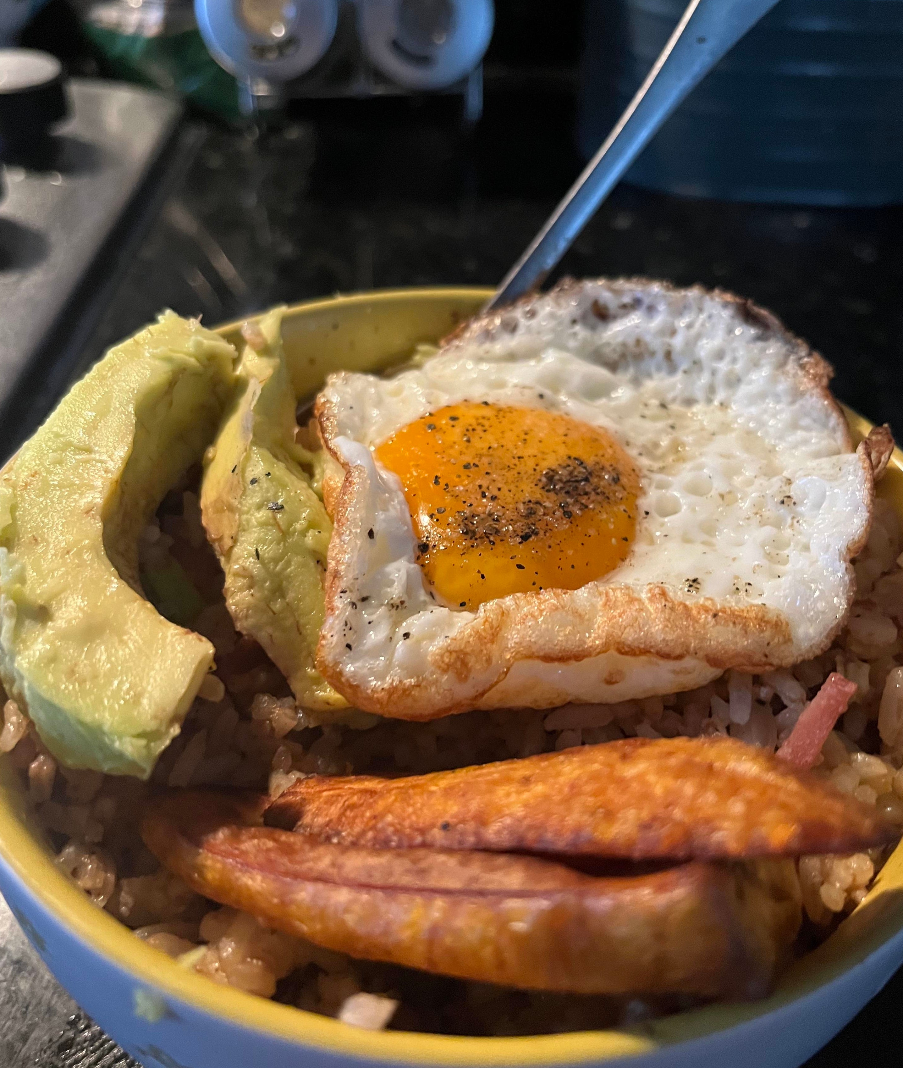 Bowl with rice, a fried egg on top, avocado slices, and fried plantains on the side