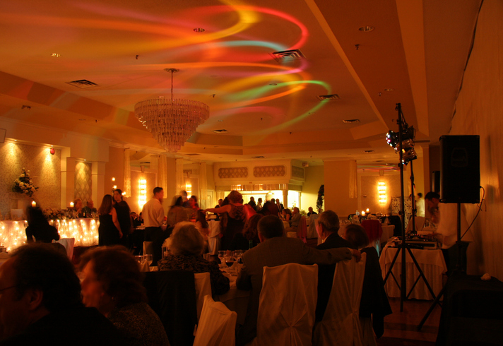 People socializing in a banquet hall with a chandelier and vibrant ceiling light display