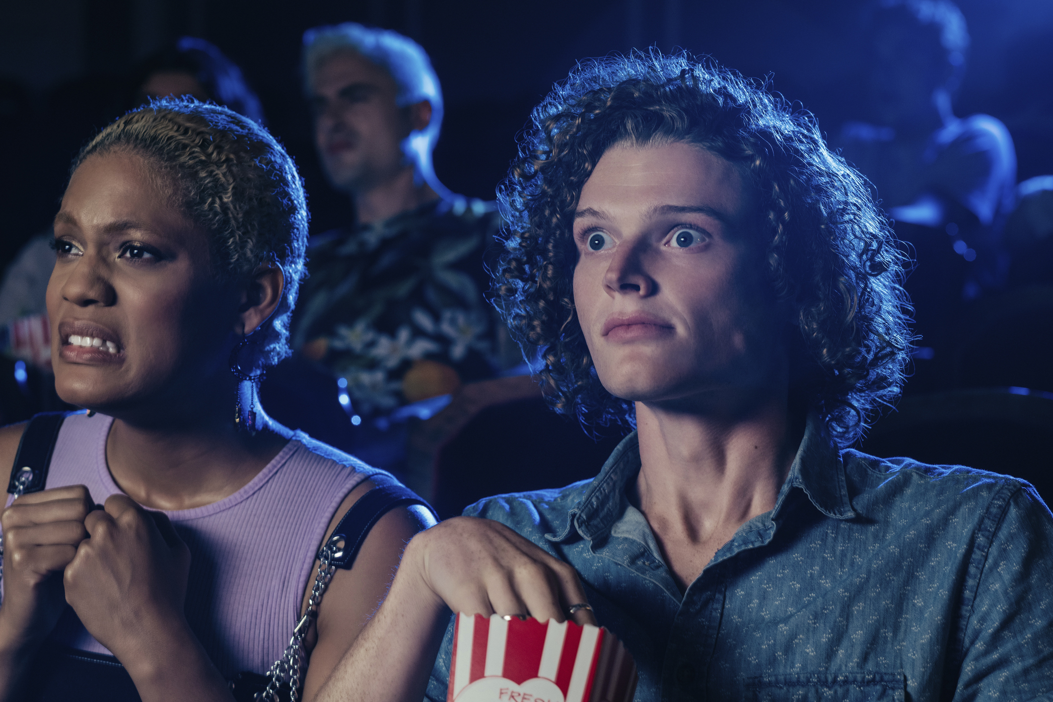 Two people in a cinema with popcorn, one person excited, another apprehensive