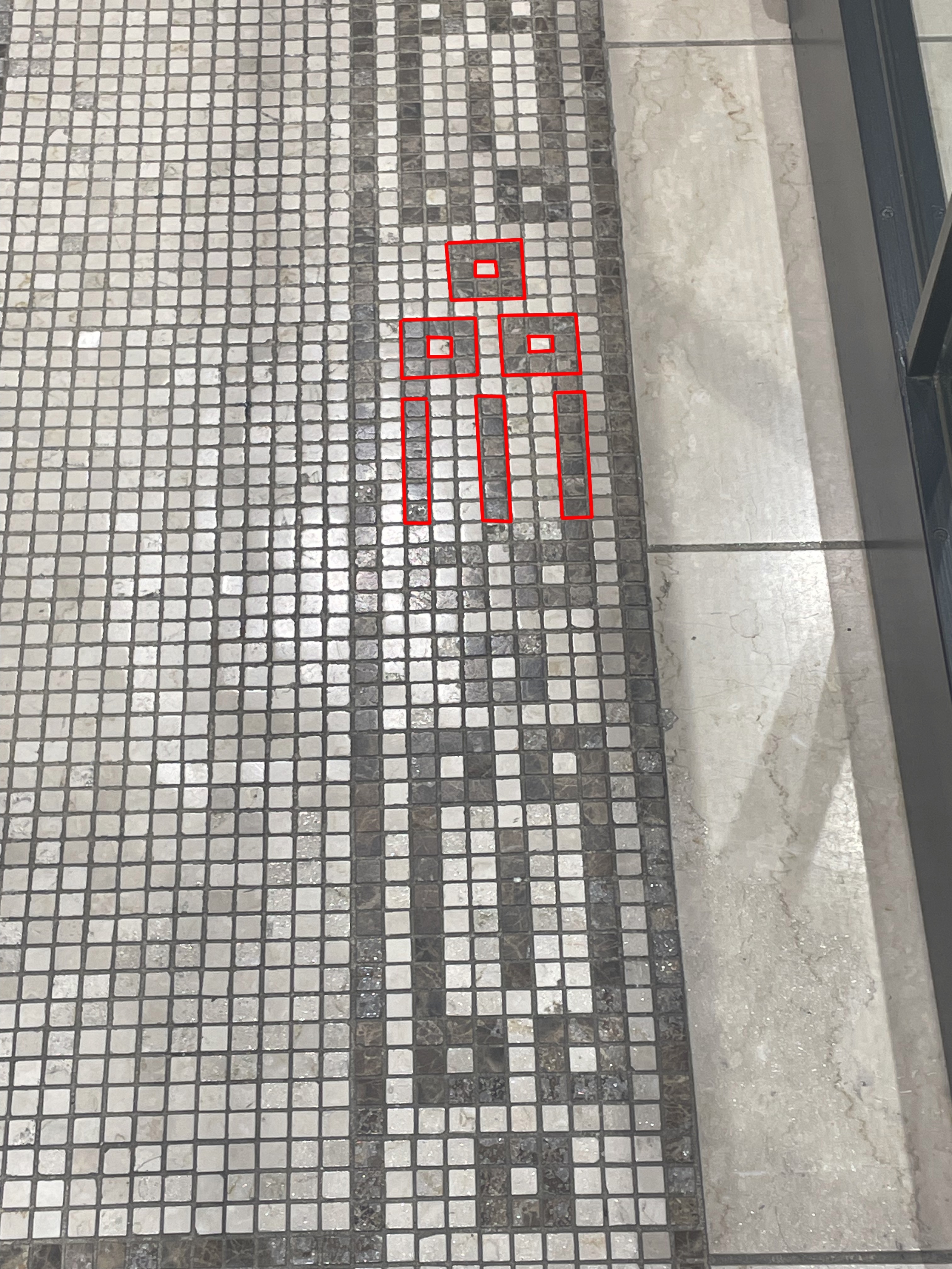 盲導用のタイルが敷かれた歩道で、赤いラインで示されたエリアに注意を促す標示がある。