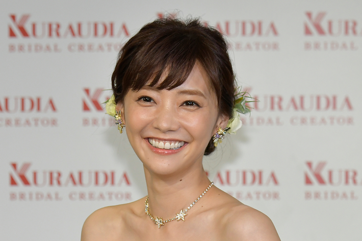 ウェディングドレスを着た女性がカメラに向かって微笑んでいる。背景には「KURAUDIA BRIDAL CREATOR」の文字がある。