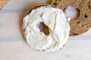 A bagel with cream cheese on one half next to an untoasted half on a table