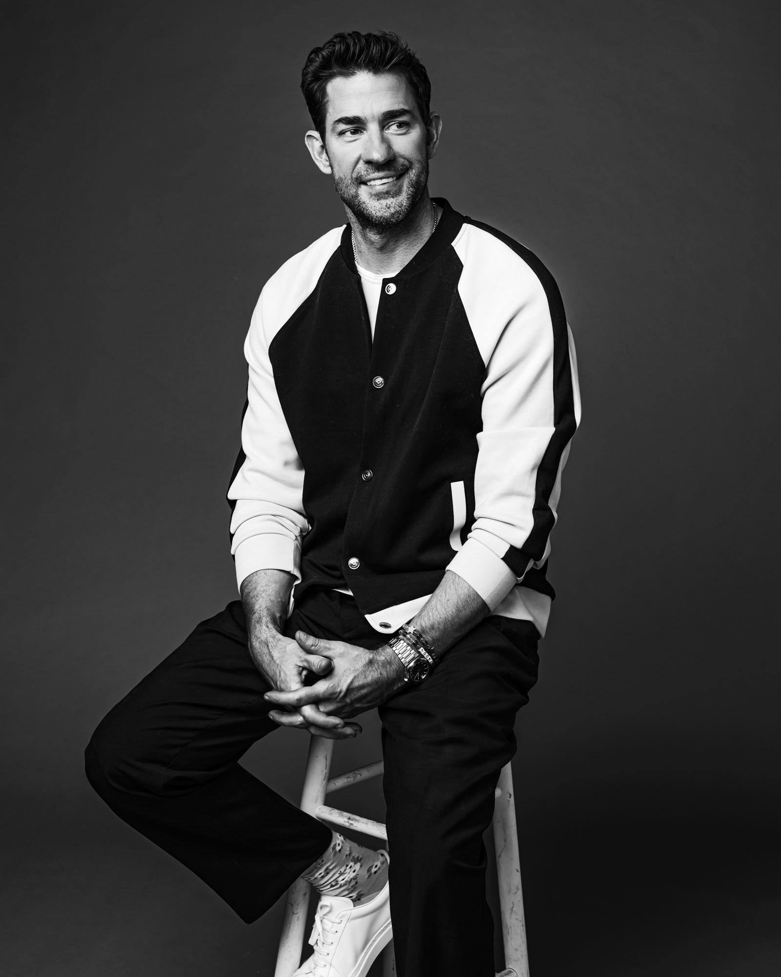 Closeup of John Krasinski sitting on a stool