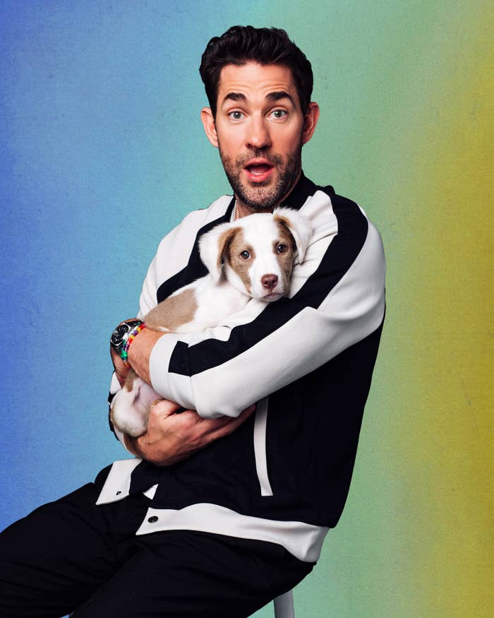 John Krasinki in a striped jacket holding a puppy against a colored backdrop