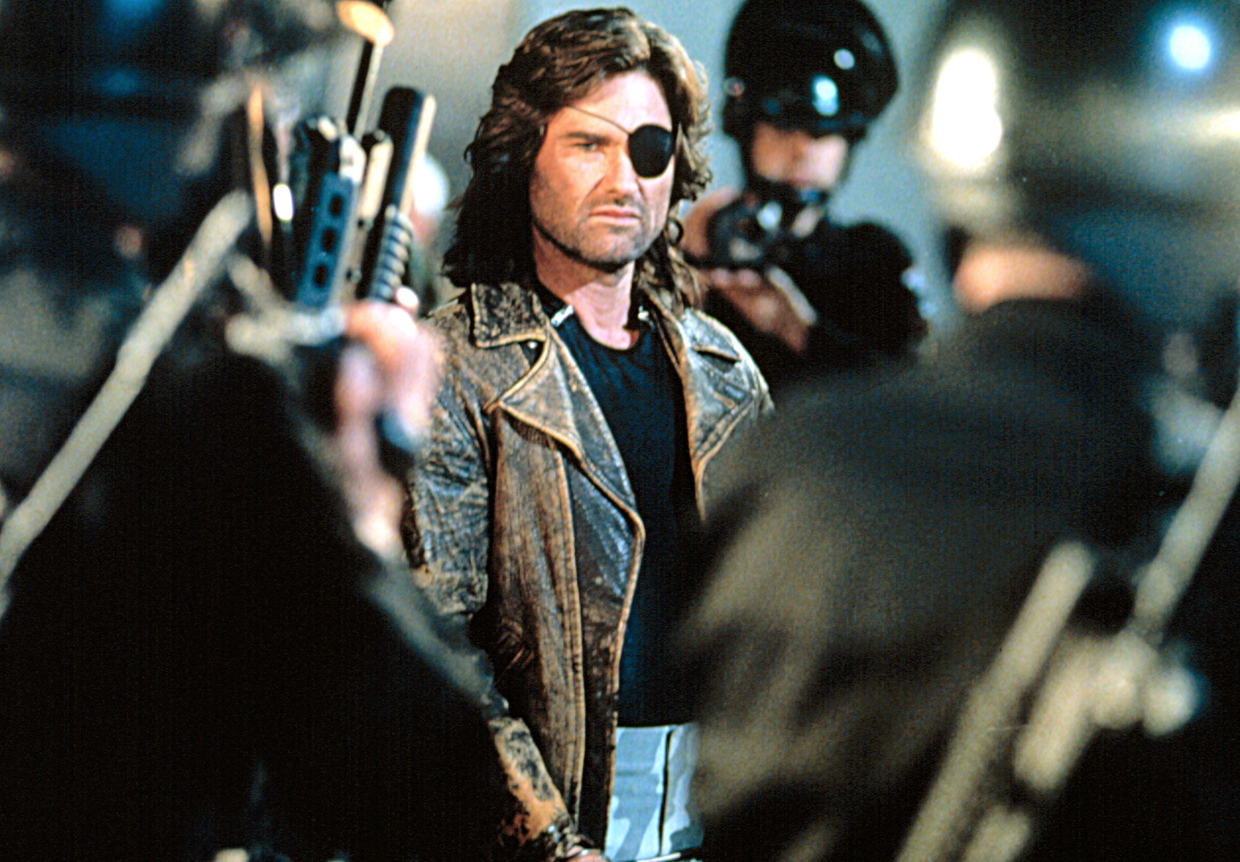 Character Snake Plissken stands defiantly surrounded by armed guards in a scene from the film &quot;Escape from New York.&quot;