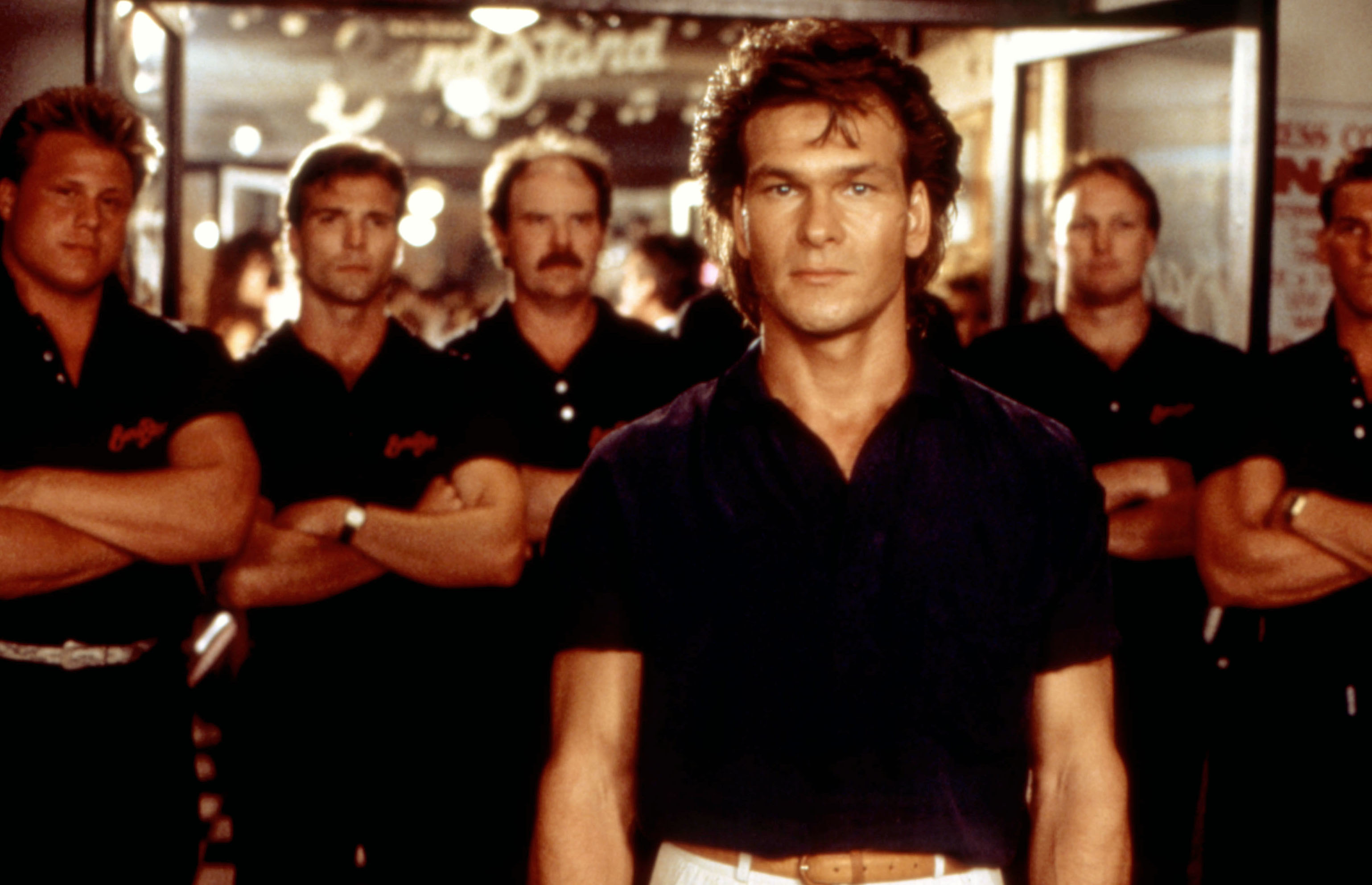 Patrick Swayze stands in front with a group in a bar in the movie &quot;Road House.&quot;