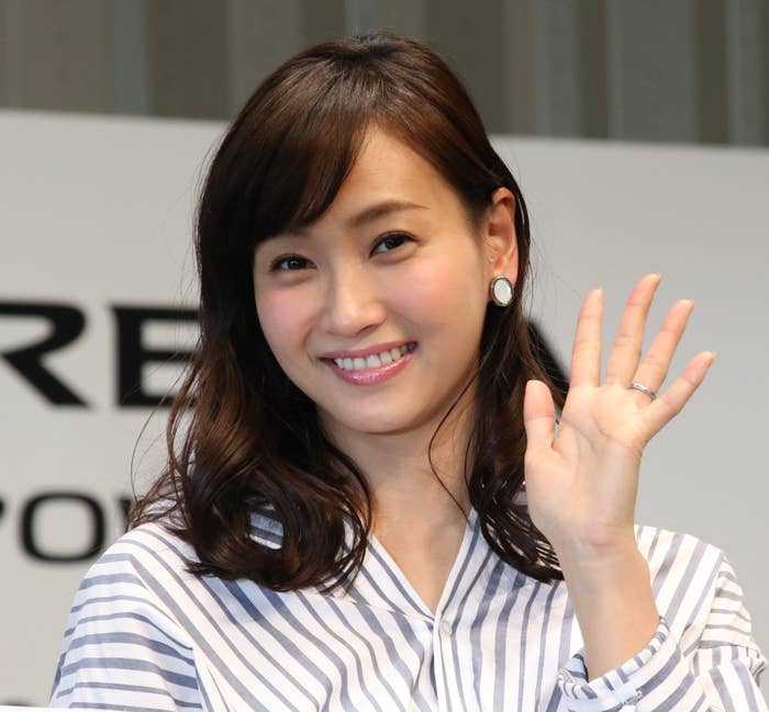 女性がカメラに向かって微笑み、手を振っています。彼女はストライプの服を着ています。