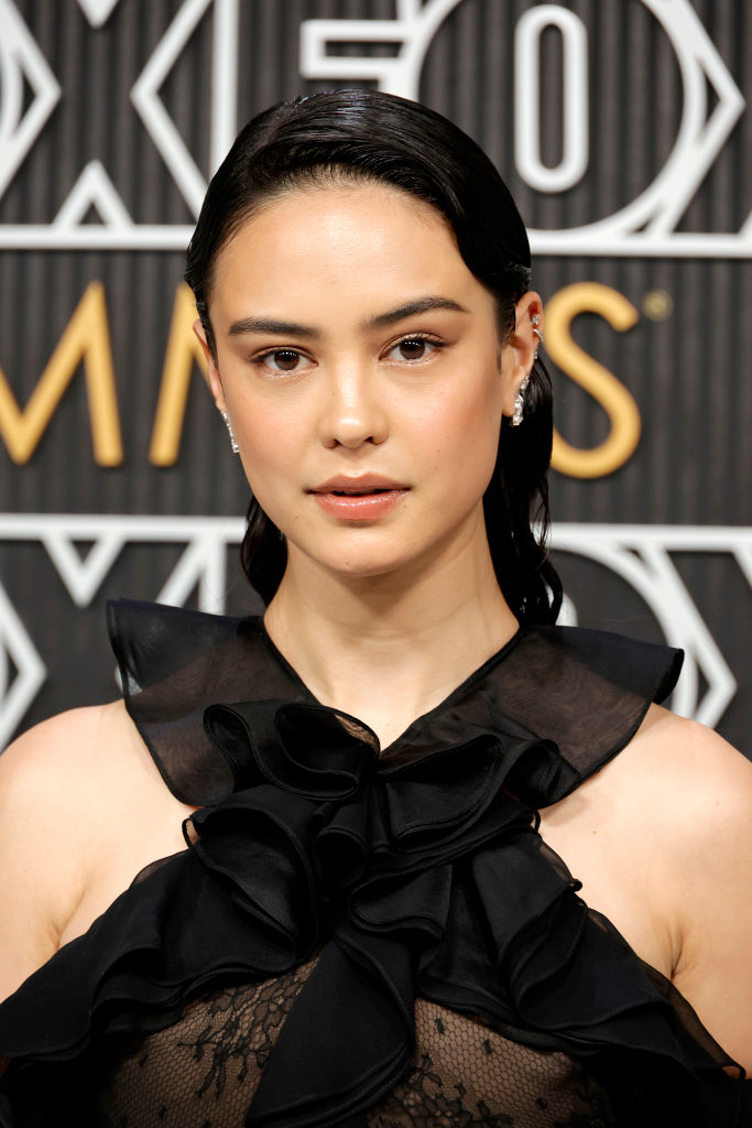 Celebrity in a black ruffled outfit posing in front of a patterned backdrop