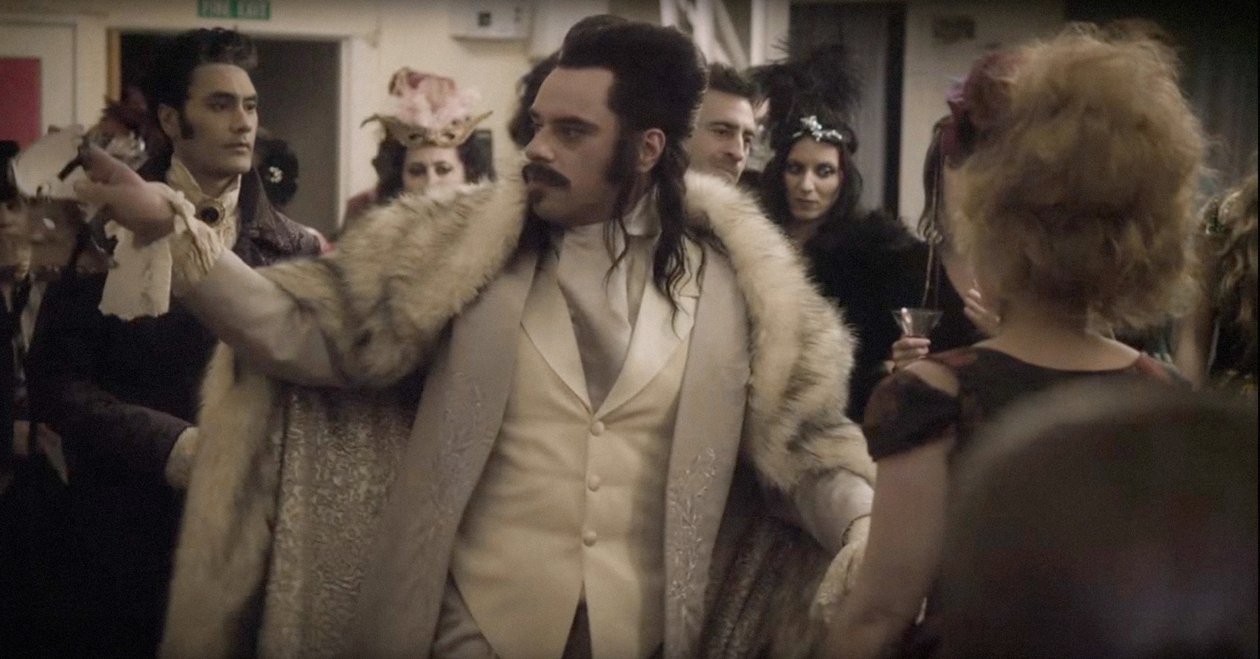 Actor in period costume with a white vest and fur coat at a masquerade party scene