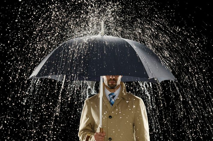 男性が傘を差し、雨が降る中を立っています。