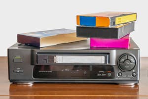 A VCR with a stack of VHS tapes on top, evoking retro technology nostalgia