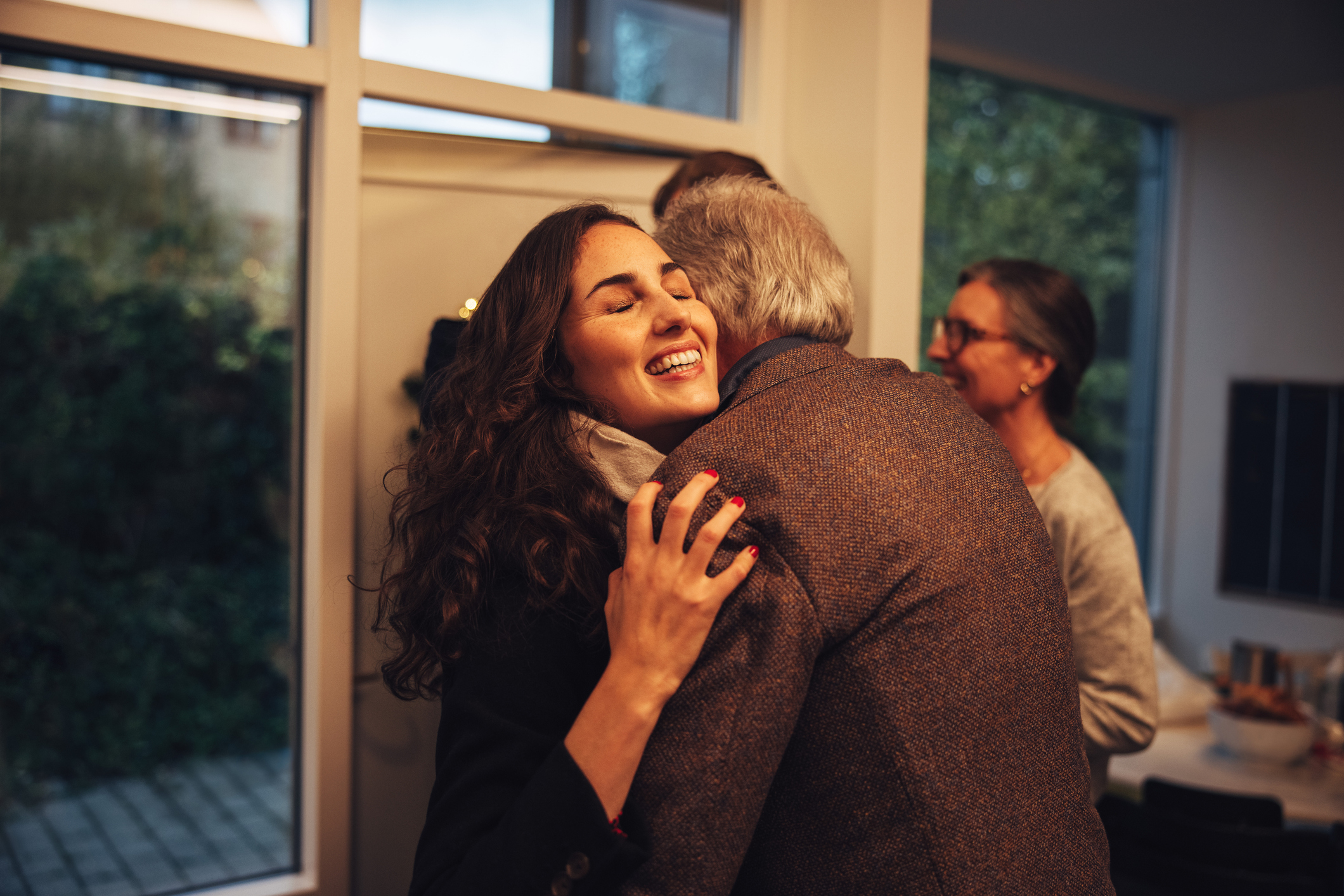 Woman embracing a man in an indoor setting, two others converse in the background