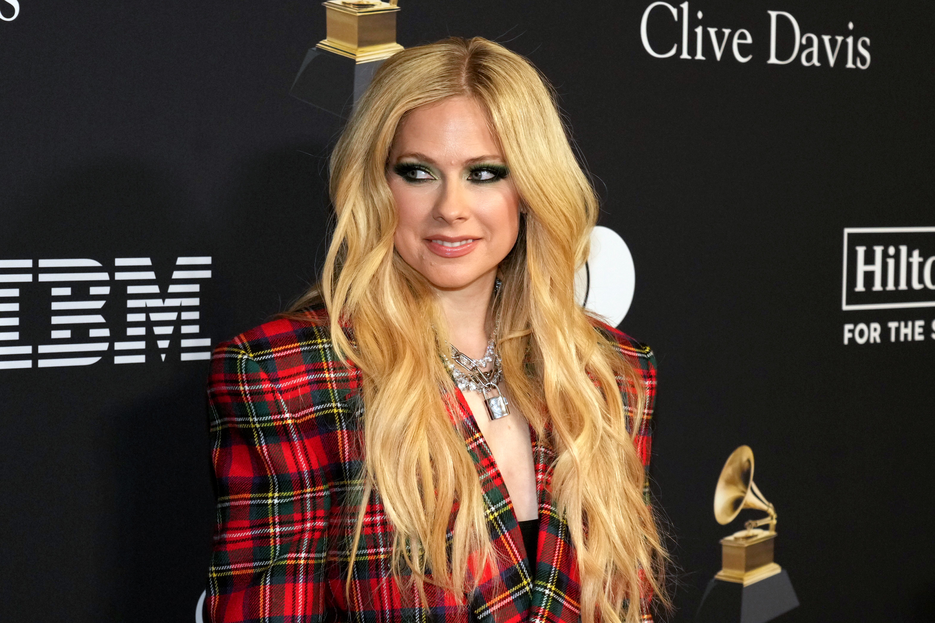 Avril Lavigne poses at an event wearing a plaid suit jacket and heavy makeup